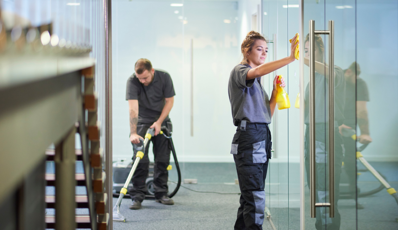 Male cleaner vacuuming and female cleaner cleaning glass in office